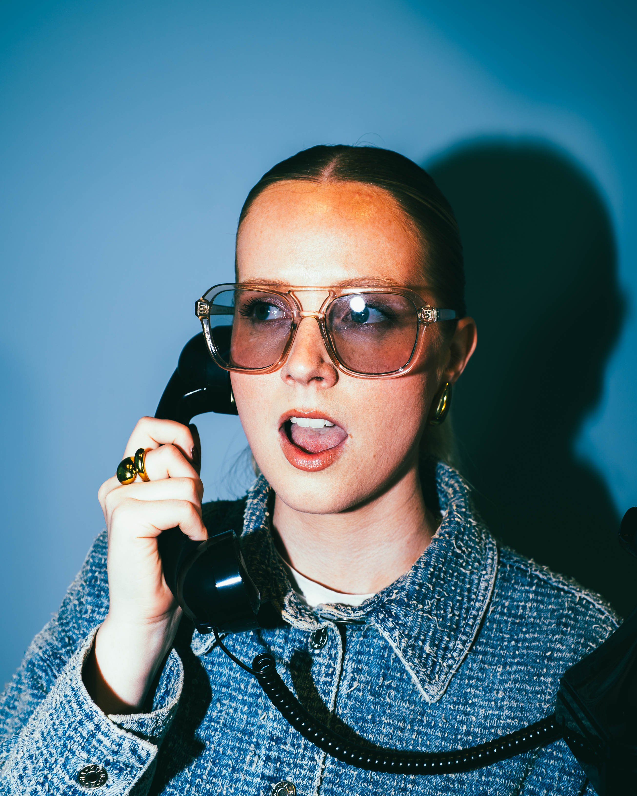 A young woman with glasses holding a black telephone.