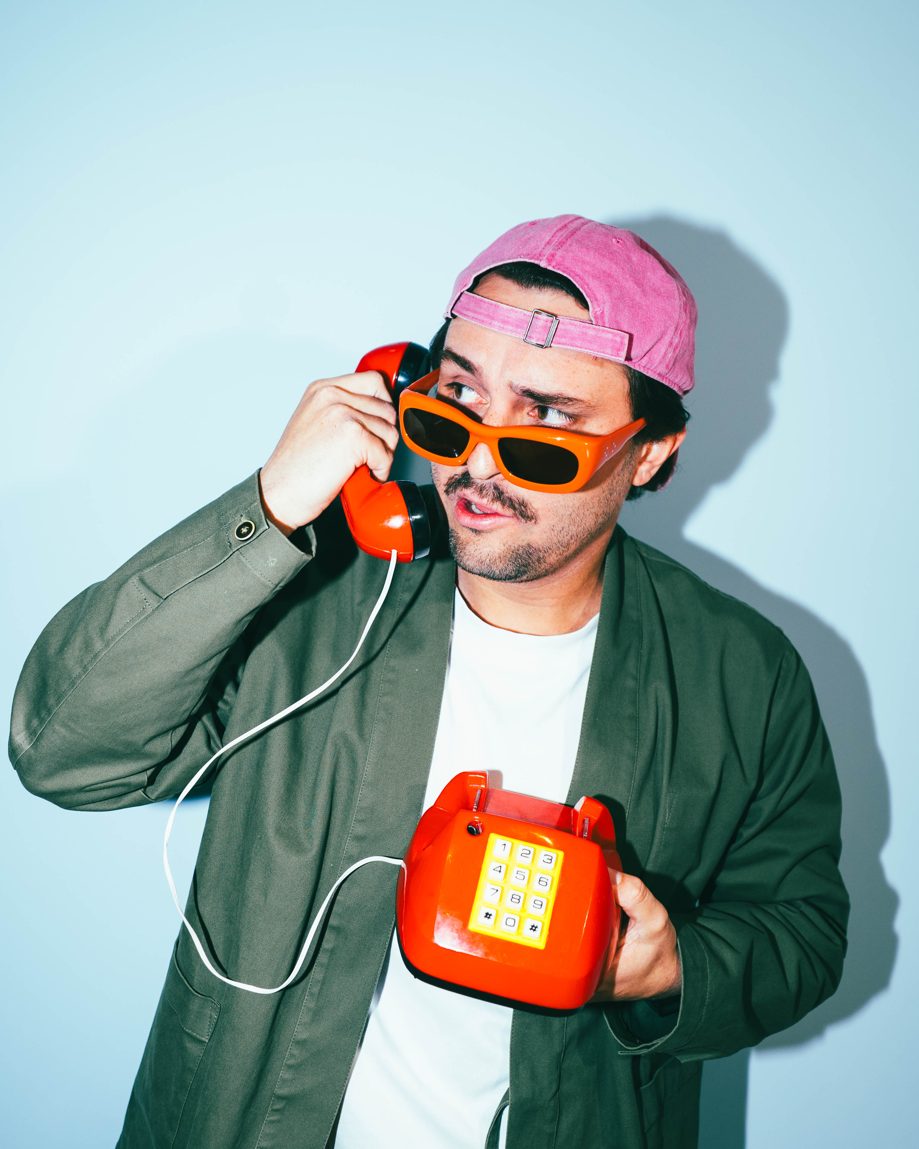 Young man with red sunglasses and a pink cap holding a red telephone.