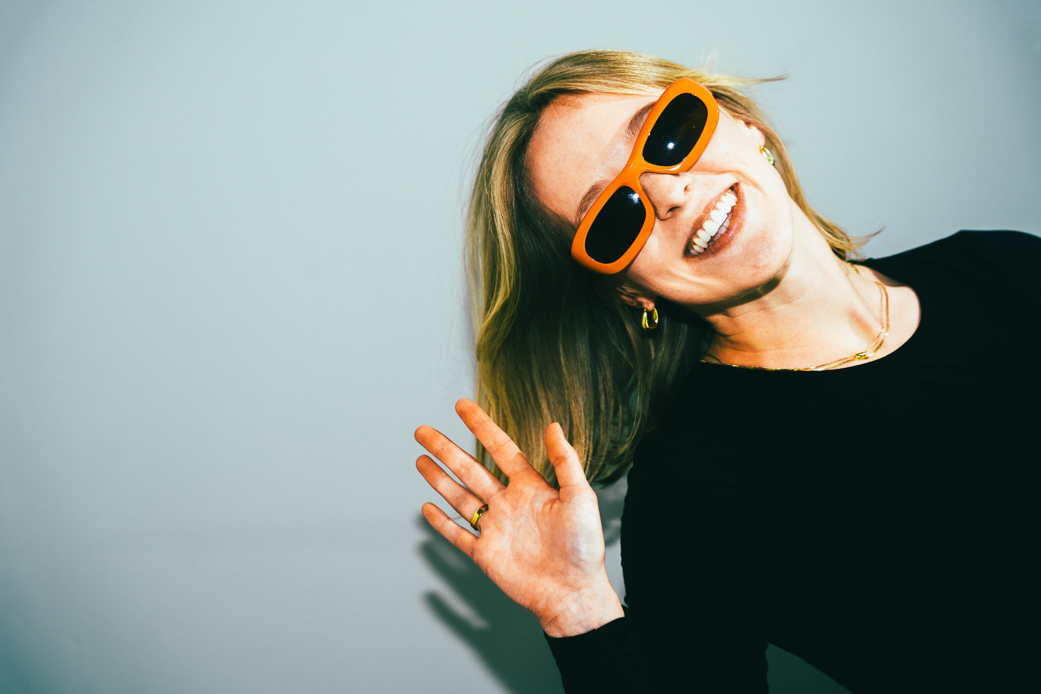 Young woman with orange sunglasses waving.