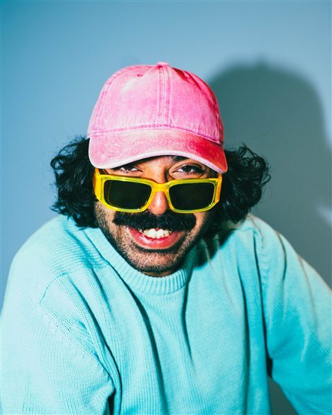 Young man smiling with yellow sunglasses and a pink cap.