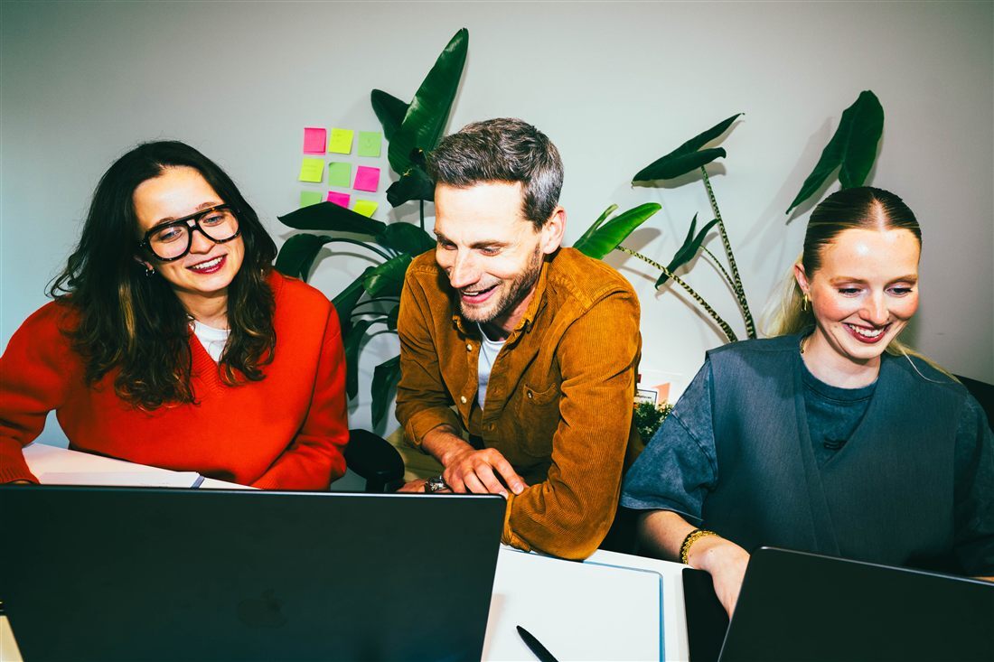 A mentor between two young people behind a laptop helping them.